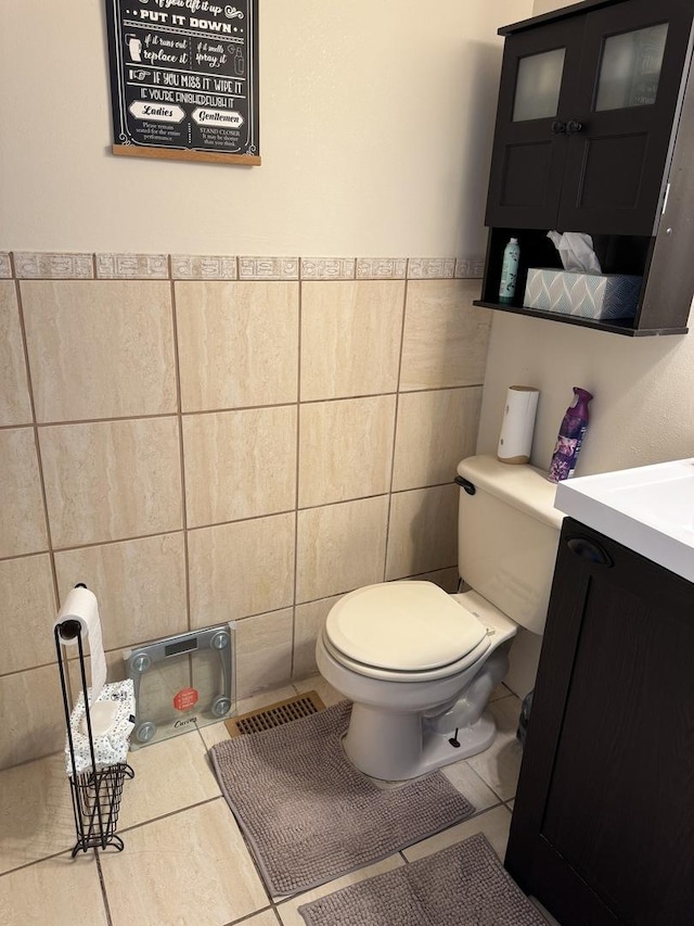 half bathroom with tile walls, toilet, tile patterned flooring, vanity, and wainscoting