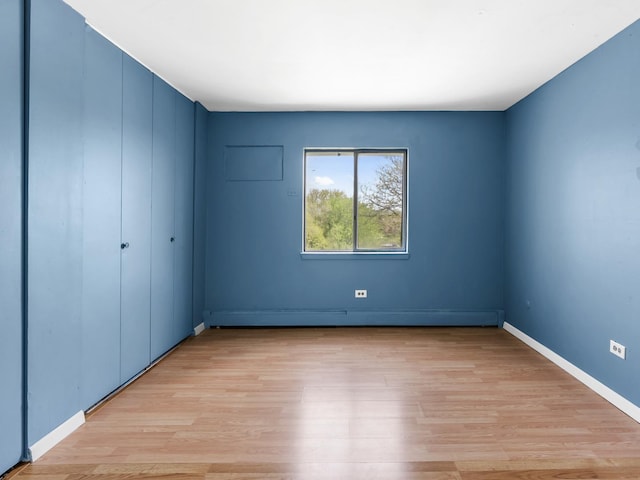 unfurnished bedroom featuring baseboard heating, light wood finished floors, baseboards, and a closet