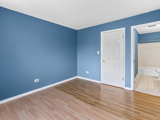 unfurnished bedroom with wood finished floors, baseboards, and ensuite bath