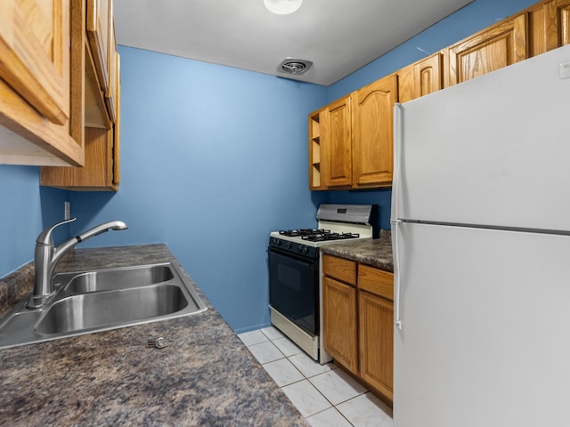 kitchen with freestanding refrigerator, gas range, a sink, dark countertops, and light tile patterned flooring