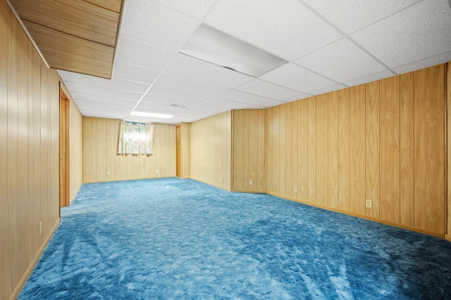 finished basement with wooden walls, carpet, and a drop ceiling