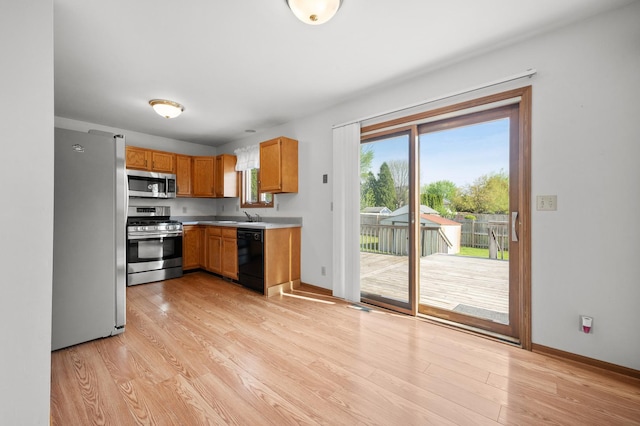 kitchen featuring stainless steel appliances, light wood finished floors, a sink, light countertops, and baseboards