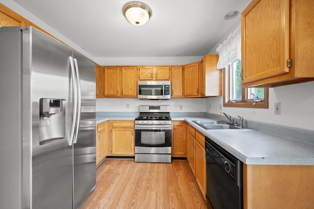 kitchen with appliances with stainless steel finishes, a sink, light wood-type flooring, and light countertops