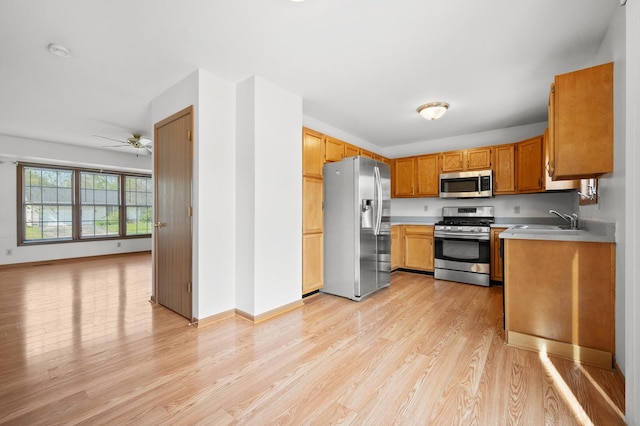 kitchen with appliances with stainless steel finishes, a sink, light wood-style flooring, light countertops, and a ceiling fan