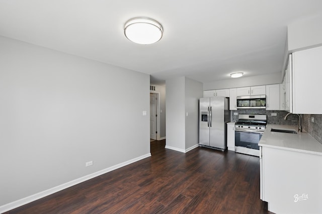 kitchen with appliances with stainless steel finishes, a sink, light countertops, tasteful backsplash, and dark wood-style floors