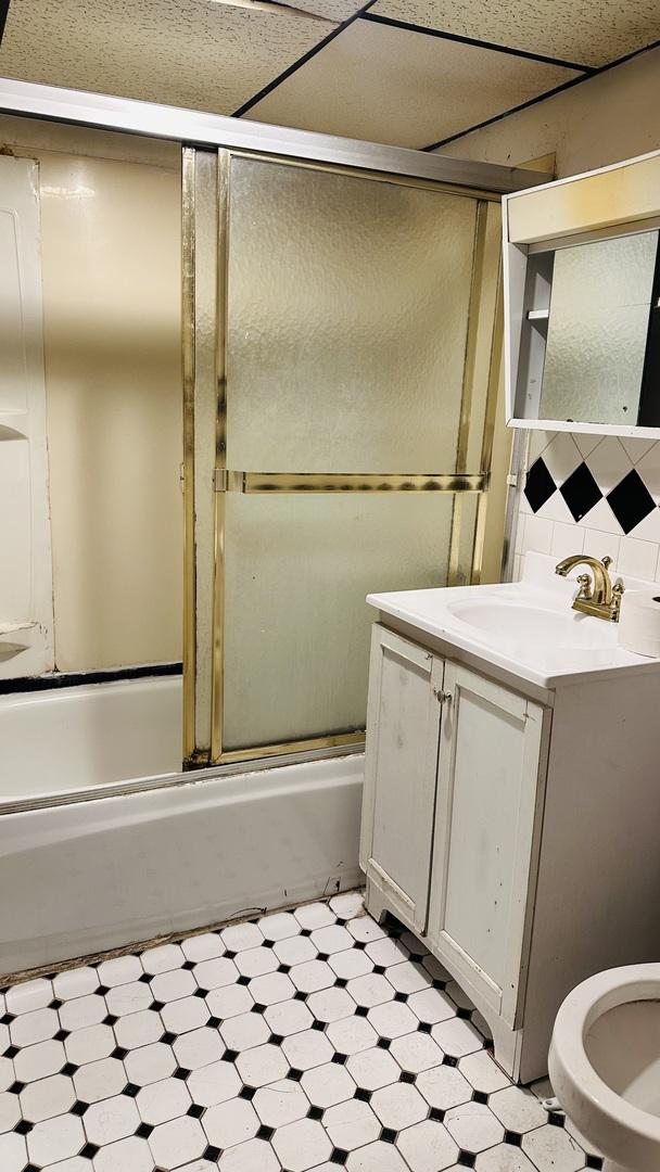 bathroom featuring tile patterned floors, enclosed tub / shower combo, vanity, backsplash, and toilet