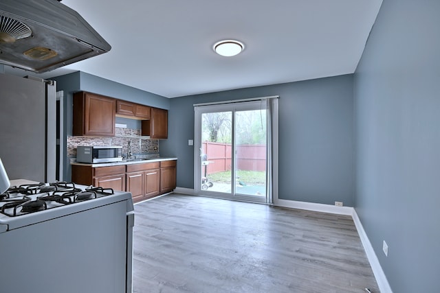 kitchen with stainless steel appliances, ventilation hood, baseboards, decorative backsplash, and light wood finished floors