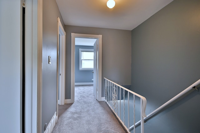 hallway featuring carpet flooring, baseboards, and an upstairs landing