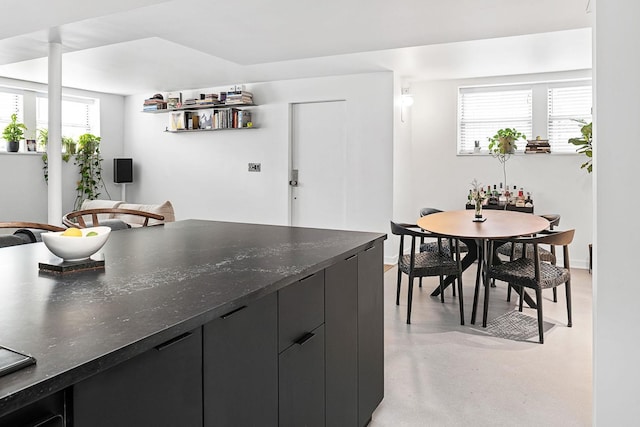 kitchen with dark cabinetry, concrete floors, baseboards, and dark stone countertops