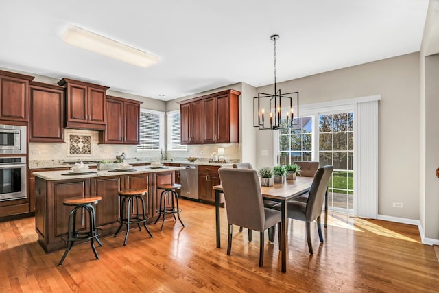 kitchen with appliances with stainless steel finishes, tasteful backsplash, a chandelier, light wood-style flooring, and a kitchen island