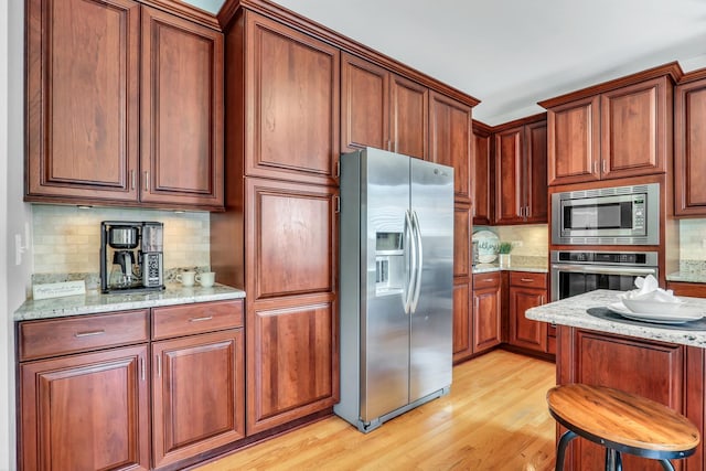 kitchen featuring stainless steel appliances, tasteful backsplash, light wood finished floors, light stone countertops, and brown cabinetry