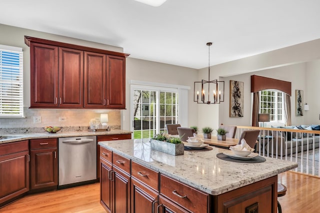 kitchen featuring stainless steel dishwasher, light wood-style floors, light stone counters, and healthy amount of natural light