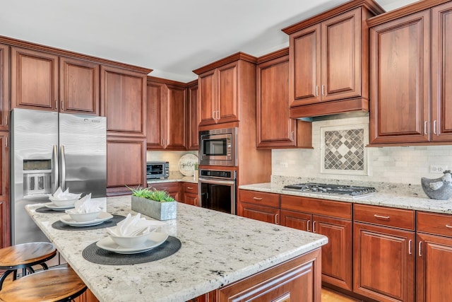 kitchen with stainless steel appliances, light stone countertops, tasteful backsplash, and a kitchen breakfast bar