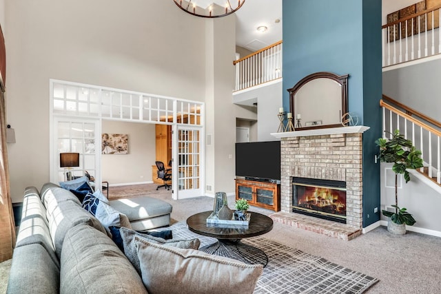 carpeted living area with a towering ceiling, french doors, baseboards, a fireplace, and stairway