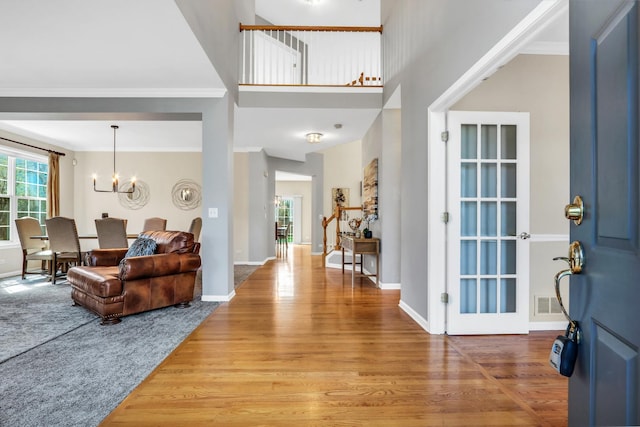 entrance foyer featuring a chandelier, light wood-style floors, ornamental molding, baseboards, and a high ceiling