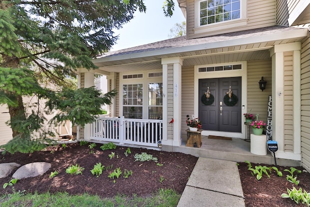 view of exterior entry with covered porch and a shingled roof
