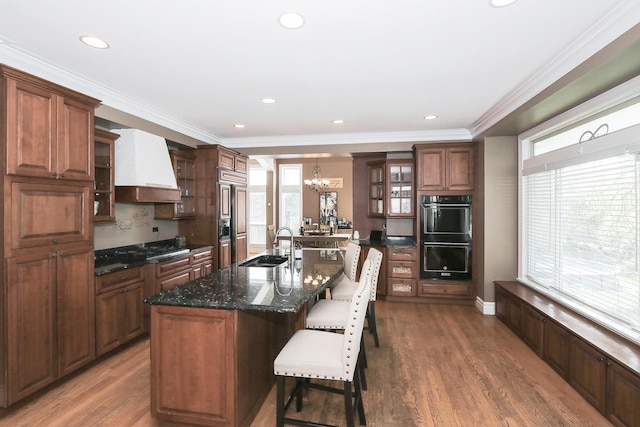 kitchen with premium range hood, a kitchen breakfast bar, a chandelier, glass insert cabinets, and wood finished floors