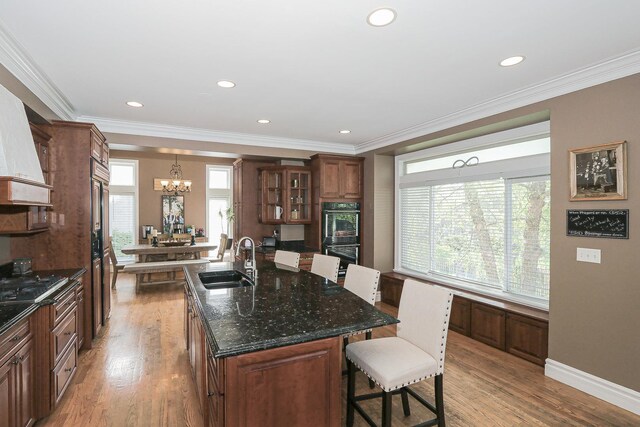 kitchen with a sink, a kitchen bar, a chandelier, light wood-type flooring, and black appliances
