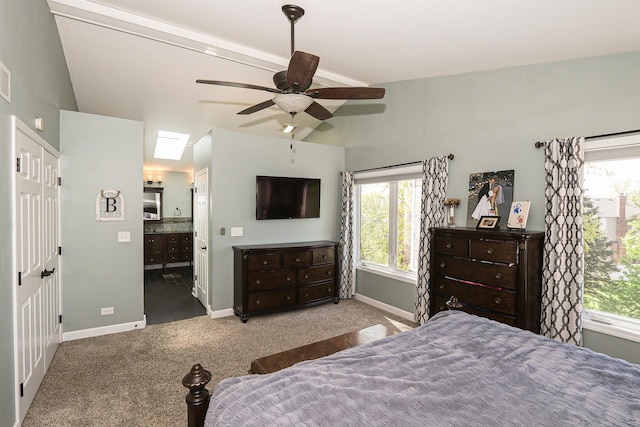 carpeted bedroom featuring baseboards, multiple windows, ensuite bath, vaulted ceiling, and a ceiling fan