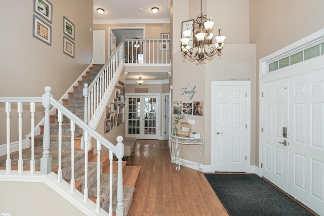 foyer with a high ceiling, stairs, crown molding, french doors, and wood finished floors