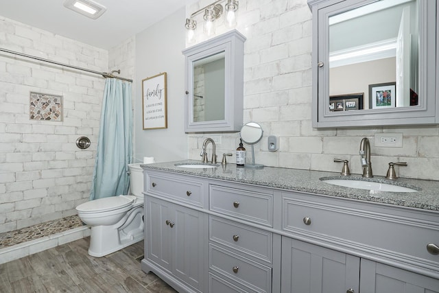 full bath featuring tiled shower, double vanity, toilet, and wood finished floors