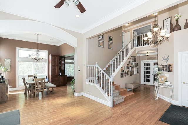 stairs with a chandelier, a ceiling fan, arched walkways, wood finished floors, and plenty of natural light