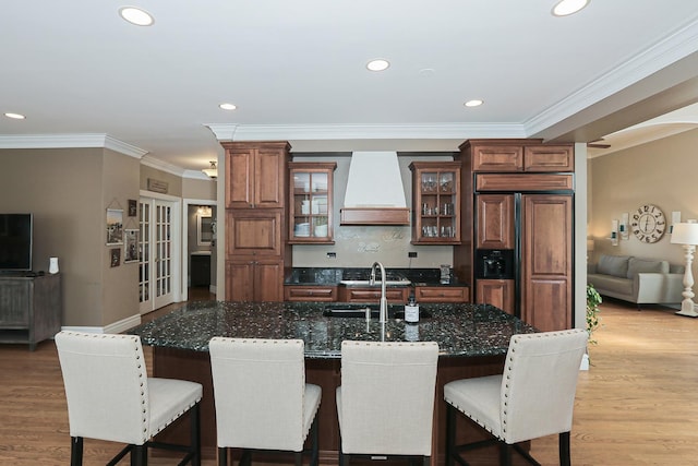 kitchen featuring custom exhaust hood, paneled built in refrigerator, a breakfast bar, crown molding, and glass insert cabinets