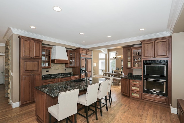 kitchen with wall chimney exhaust hood, paneled fridge, a sink, a breakfast bar, and a chandelier