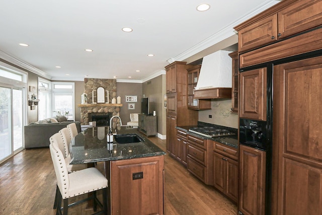 kitchen featuring a sink, premium range hood, paneled fridge, crown molding, and a breakfast bar area