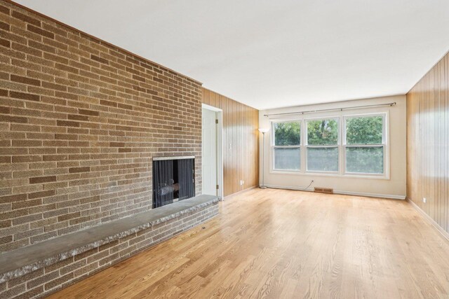 unfurnished living room with a fireplace, wood finished floors, baseboards, and brick wall