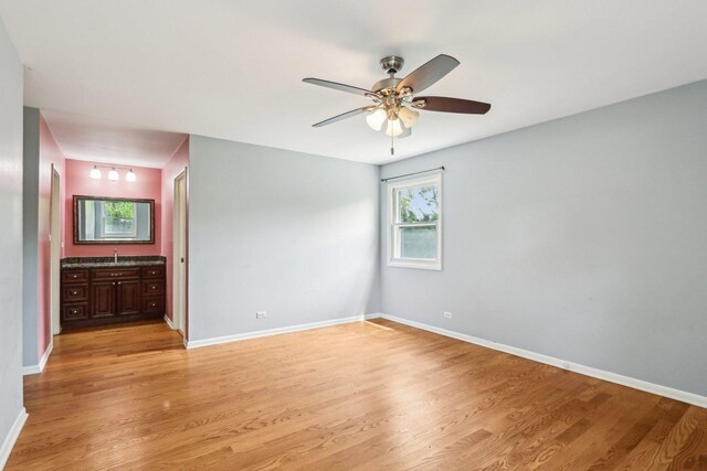 unfurnished bedroom with light wood-style flooring, baseboards, a sink, and ensuite bathroom