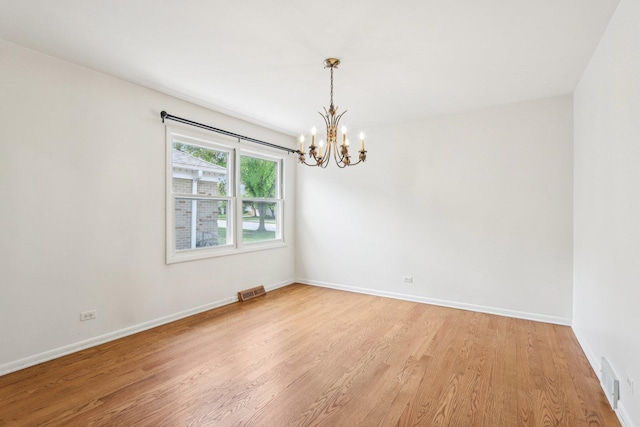 empty room featuring a chandelier, light wood-type flooring, and baseboards