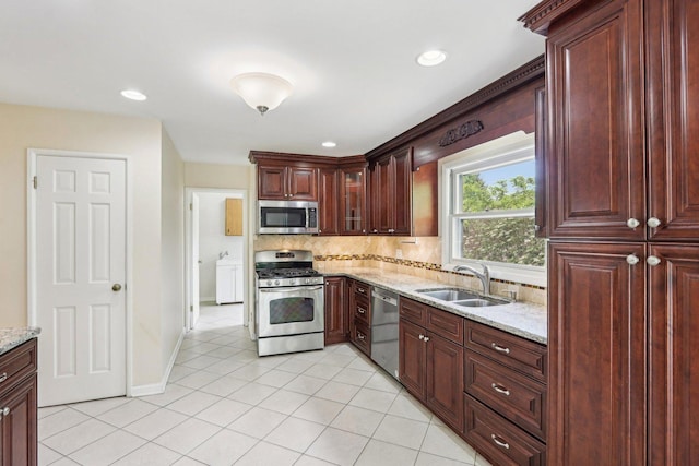 kitchen featuring appliances with stainless steel finishes, a sink, decorative backsplash, light tile patterned flooring, and light stone countertops