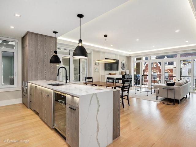 kitchen featuring a sink, wine cooler, light wood-style flooring, modern cabinets, and decorative light fixtures
