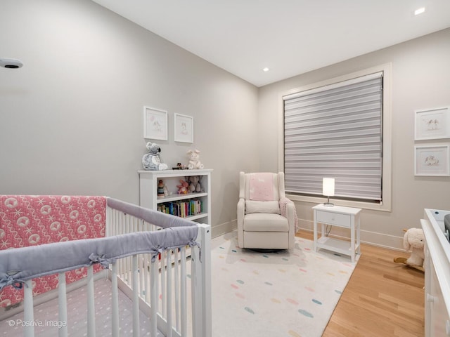 bedroom with wood finished floors, a crib, baseboards, and recessed lighting