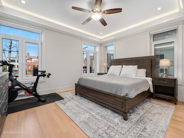 bedroom with a raised ceiling, wood finished floors, multiple windows, baseboards, and recessed lighting