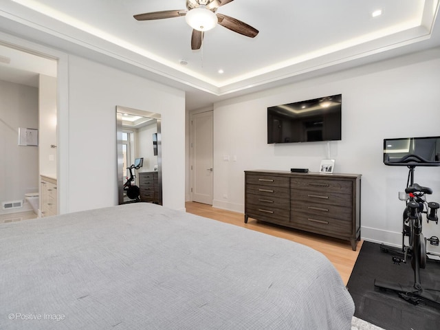 bedroom with light wood finished floors, connected bathroom, a tray ceiling, ceiling fan, and baseboards