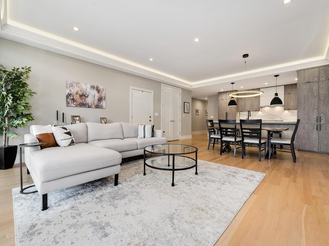 living area with a tray ceiling, light wood-type flooring, recessed lighting, and baseboards