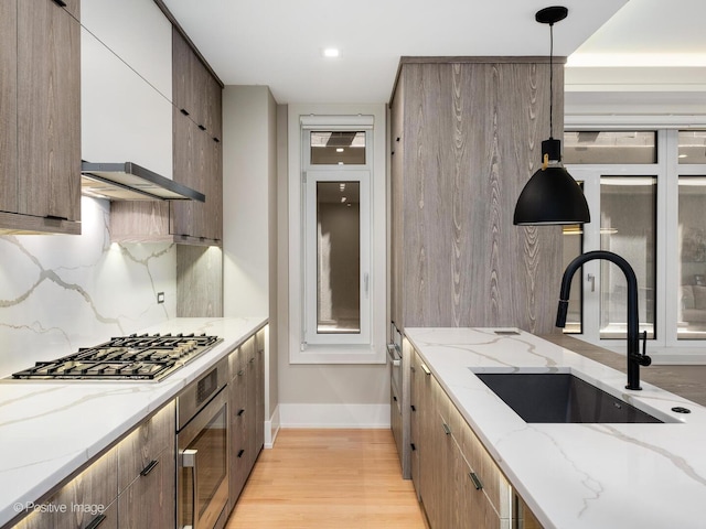 kitchen featuring a sink, appliances with stainless steel finishes, tasteful backsplash, baseboards, and light wood-style floors