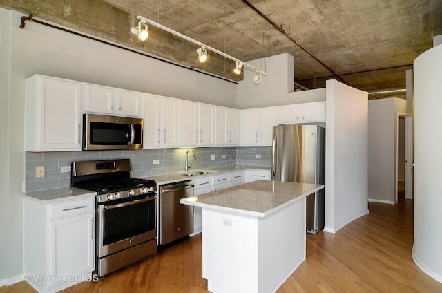 kitchen featuring stainless steel appliances, a sink, backsplash, and wood finished floors