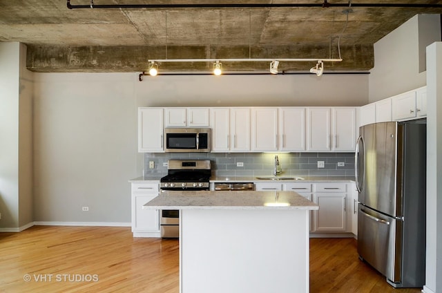kitchen with stainless steel appliances, a sink, light wood-type flooring, decorative backsplash, and a kitchen island