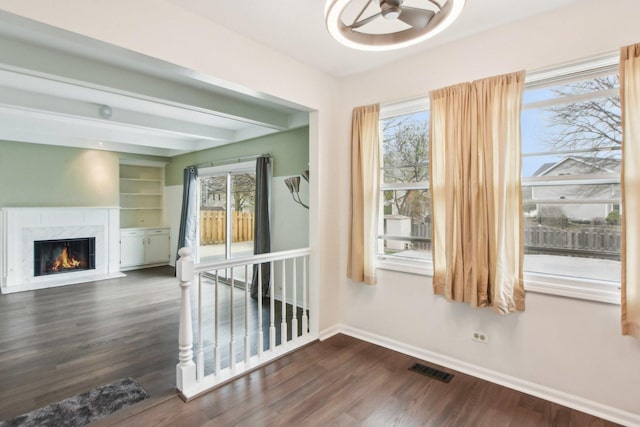 unfurnished living room with healthy amount of natural light, baseboards, a premium fireplace, dark wood finished floors, and beam ceiling