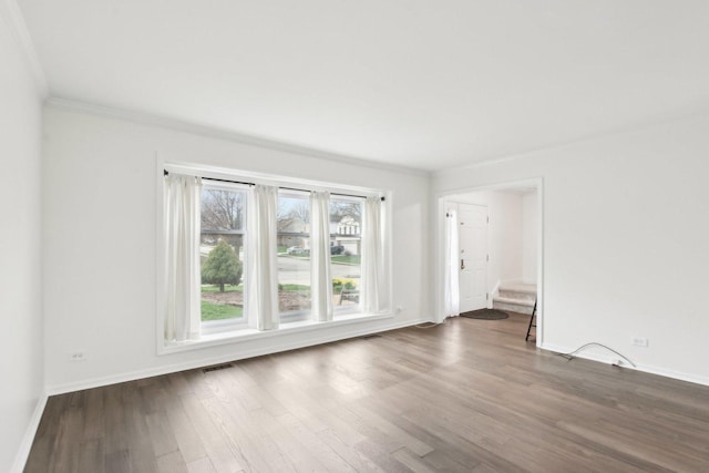 empty room with dark wood-style flooring, crown molding, and baseboards