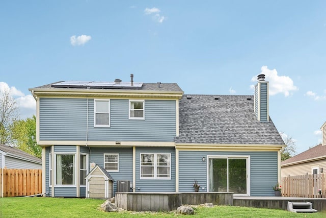 back of house with solar panels, a chimney, central air condition unit, and a shingled roof