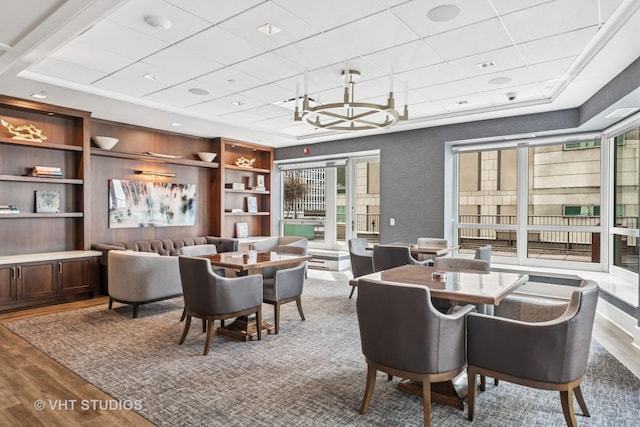 dining area with healthy amount of natural light, wood finished floors, a drop ceiling, a chandelier, and built in features
