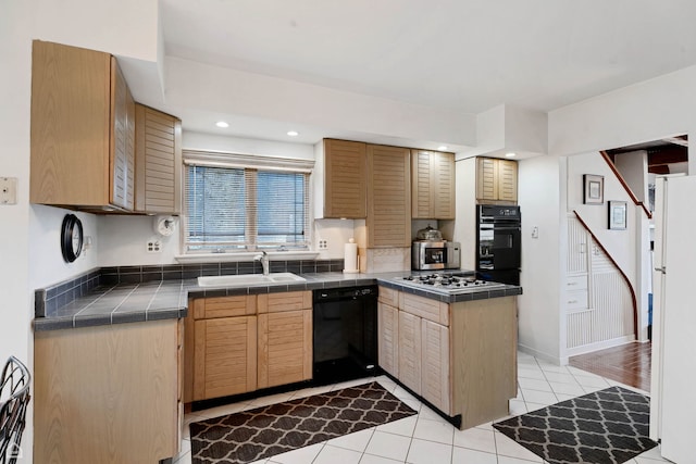kitchen with black appliances, tile counters, a sink, light tile patterned flooring, and a peninsula