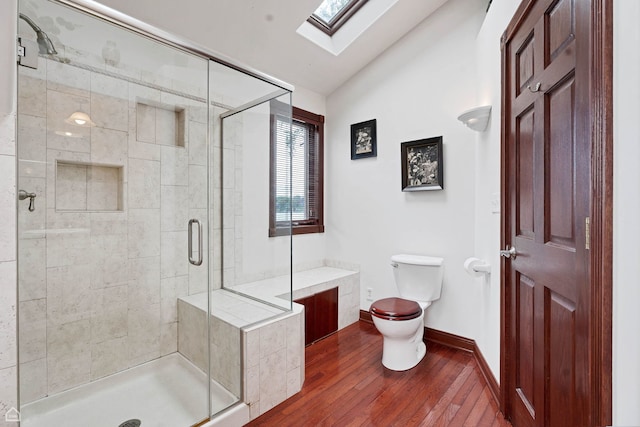 bathroom featuring wood finished floors, a skylight, vaulted ceiling, a shower stall, and toilet