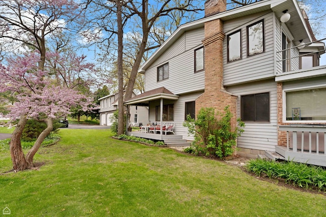 back of property featuring a chimney, a lawn, a garage, and a deck