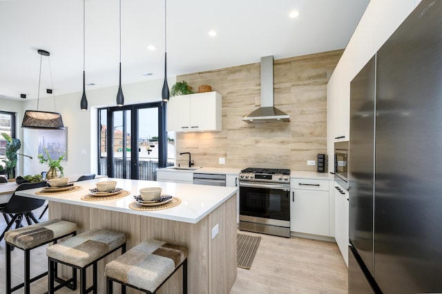kitchen with appliances with stainless steel finishes, wall chimney range hood, tasteful backsplash, light countertops, and a breakfast bar