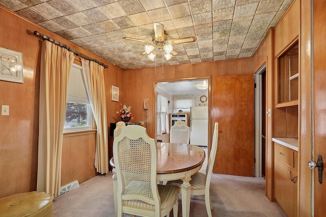 dining room with light colored carpet, an ornate ceiling, ceiling fan, and wooden walls